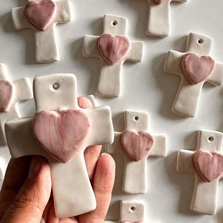 a hand holding a pink and white ceramic cross with heart shapes on it's sides