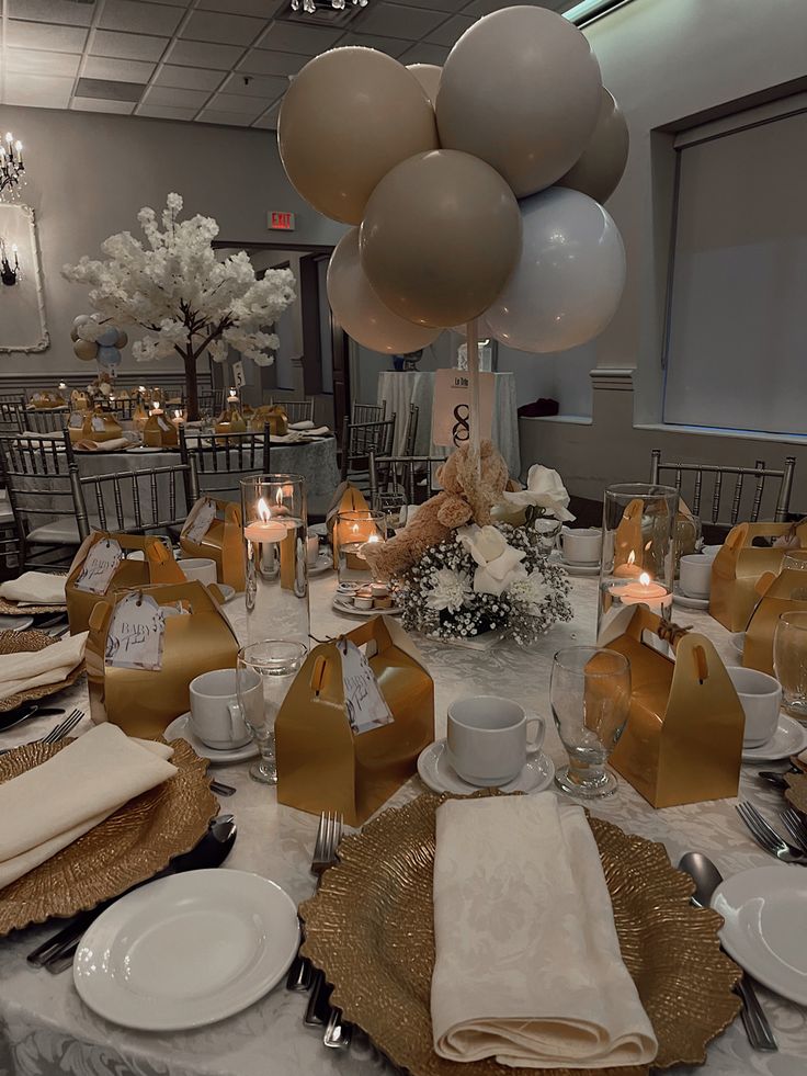 the table is set with gold and white plates, napkins, silverware, and balloons