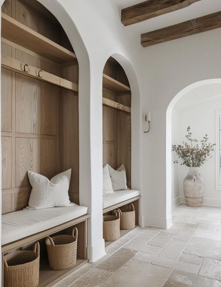 an arched entryway with benches and baskets on the floor, along with two vases filled with flowers