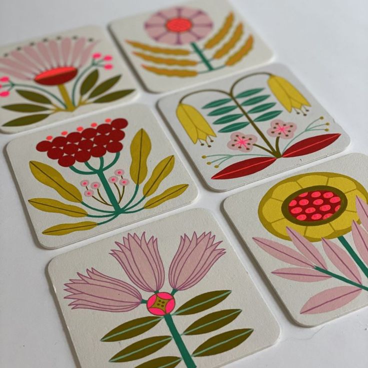 four square coasters with flowers on them sitting on a white table top next to each other