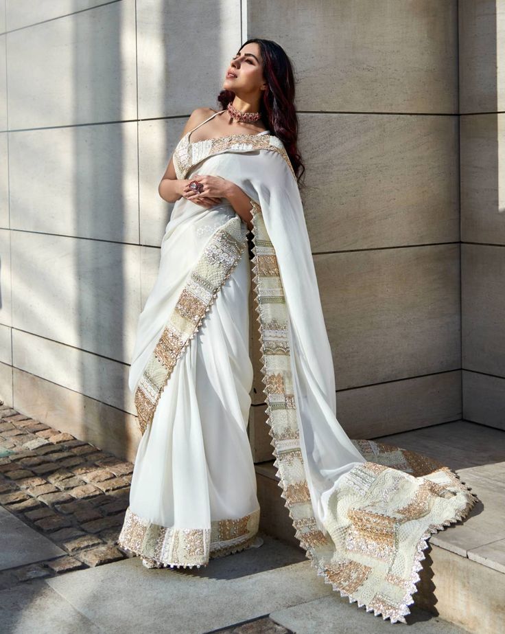 Editor's Note Featuring an ivory georgette saree enhanced with gold multi patch embroidered border, paired with a silk bralette. Fabric: Sari: georgette, bralette: dupion silk Color: Ivory, gold Component: Sari and bralette Sleeve type: sleeveless Neckline: Sweetheart Occasion: Festive Care: Dry Clean Only About the Designer Varun’s work marries the beauty of heritage Indian handcrafted embroideries with a modern colour sensibility. His clothes range from traditional saris and lehenga ensembles Gold Saree With Embroidered Border For Reception, White Silk Pre-draped Saree With Zari Work, White Chinon Saree Set, White Silk Saree With Traditional Drape, White Embroidered Lehenga For Festivals, White Pre-draped Saree With Embroidered Border For Diwali, White Silk Pre-draped Saree In Traditional Style, White Silk Pre-draped Saree With Traditional Drape, Pre-draped Georgette Saree With Embroidered Border For Diwali