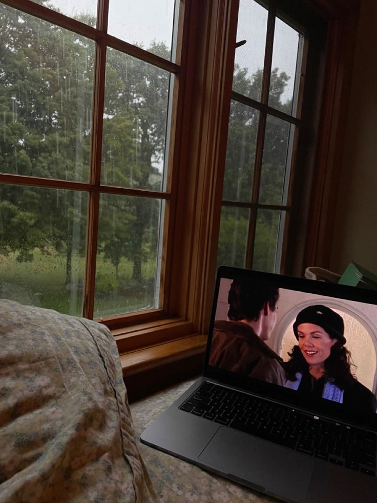 an open laptop computer sitting on top of a bed next to a window with trees in the background