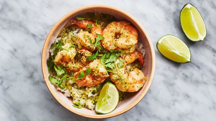 a bowl filled with shrimp and rice next to lime wedges on a marble surface