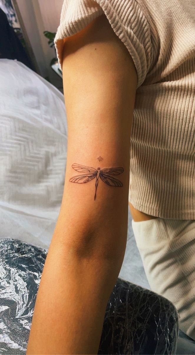 a woman's arm with a small dragonfly tattoo on the left side of her arm