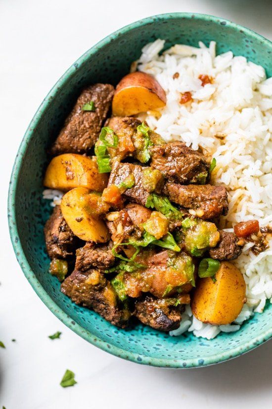 a blue bowl filled with rice and meat on top of a white countertop next to a spoon