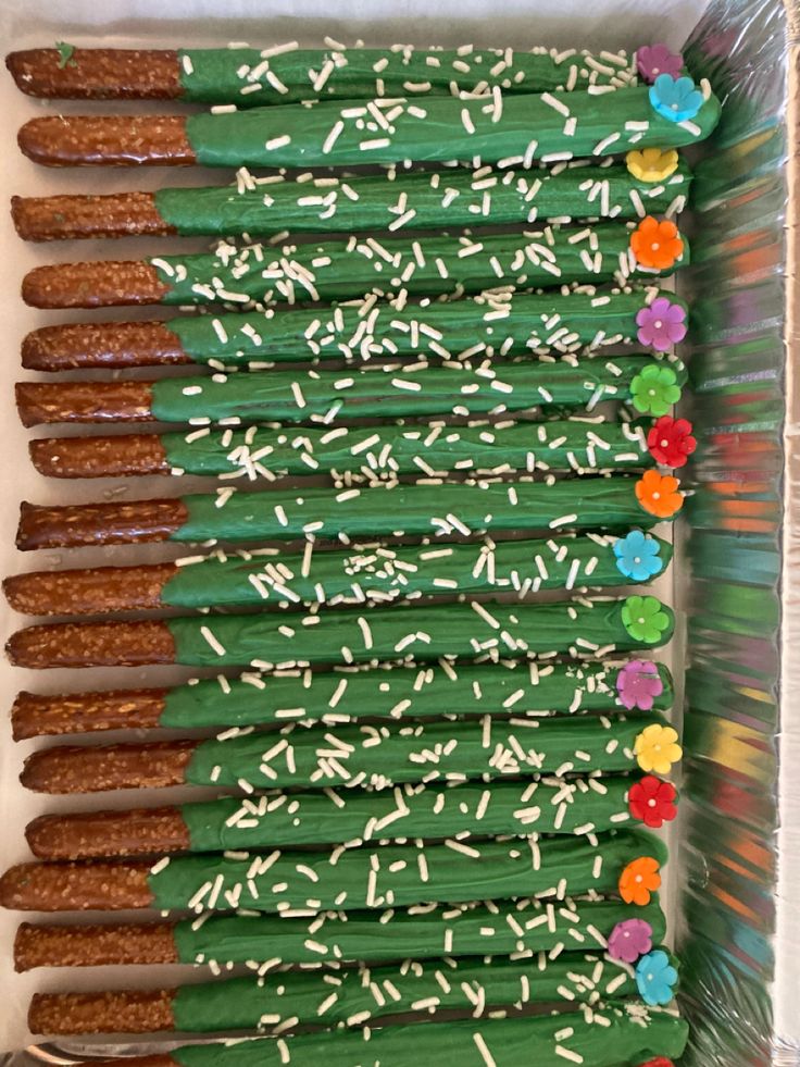 a box filled with green sticks covered in white frosting and sprinkles