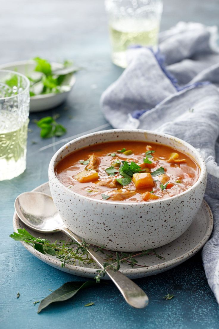 a white bowl filled with soup on top of a blue table next to two silver spoons