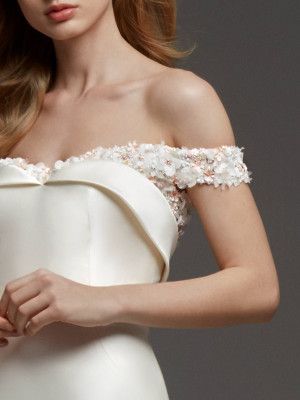 a woman in a white dress with flowers on her shoulder and shoulders, posing for the camera