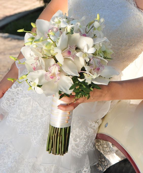 a bride holding a bouquet of white flowers in her hand and sitting on a car