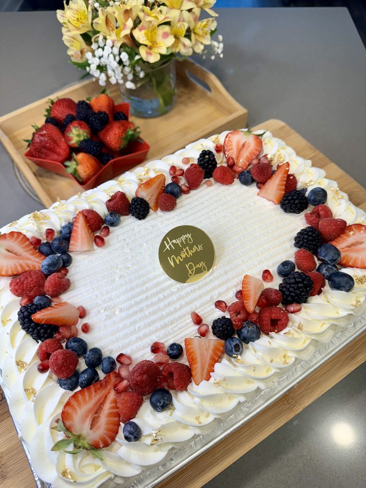 a white cake with strawberries, blueberries and raspberries on it sitting on a table