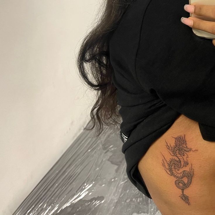 a woman with a dragon tattoo on her thigh holding a cell phone in her hand