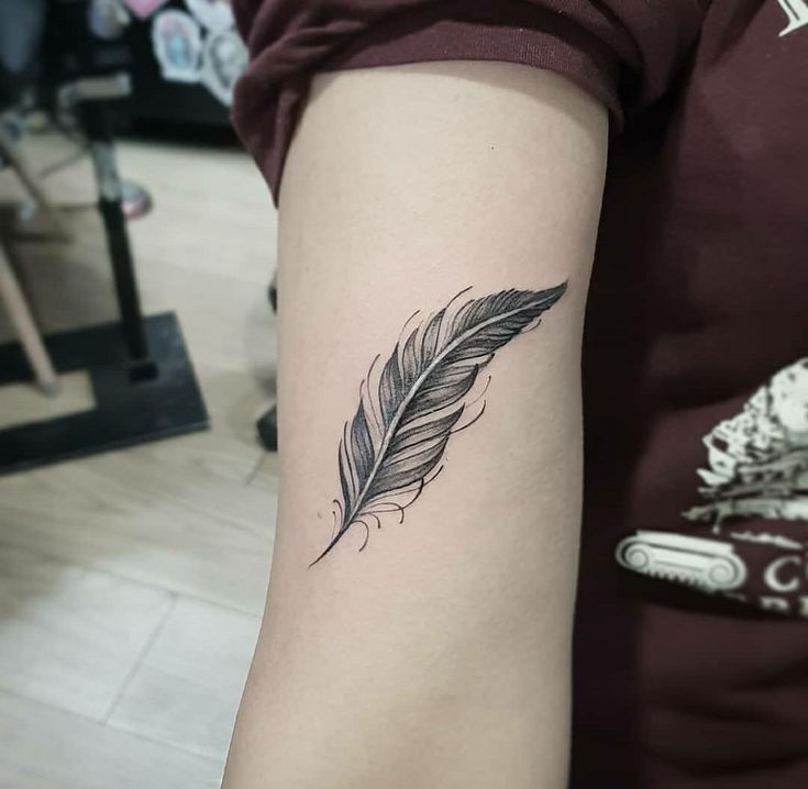 a black and white feather tattoo on the left arm by a woman's hand