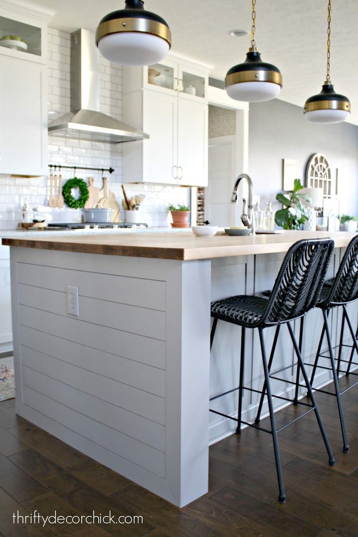 two black bar stools sitting in front of an island with three lights hanging over it