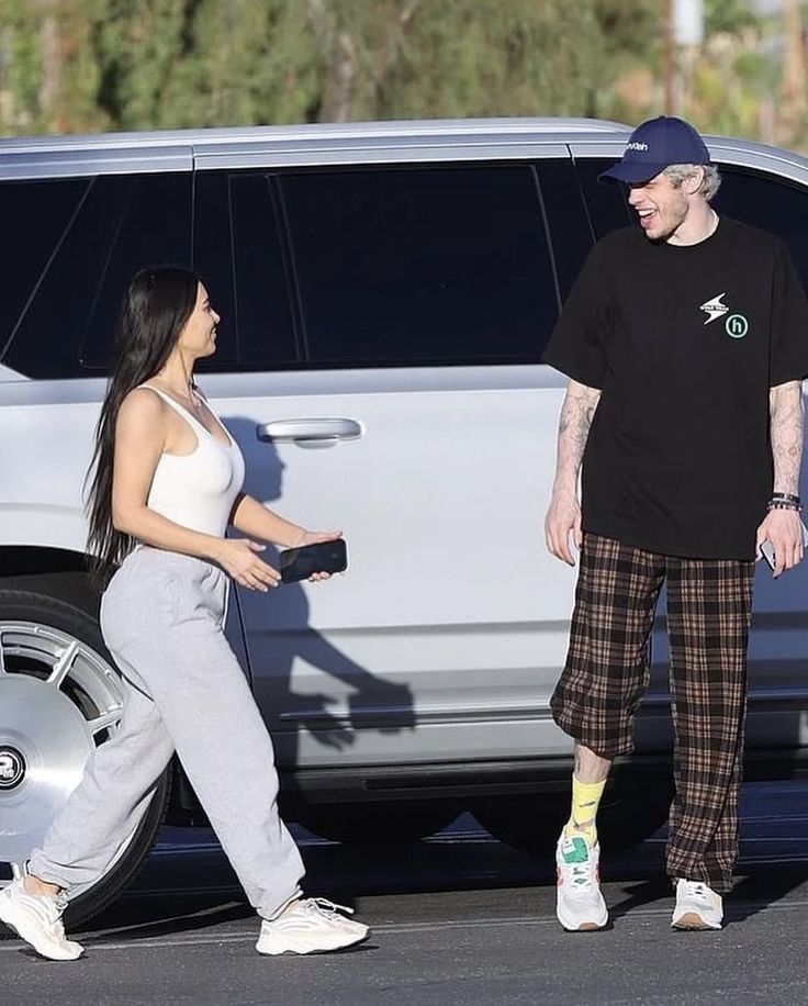 a man standing next to a woman in front of a car