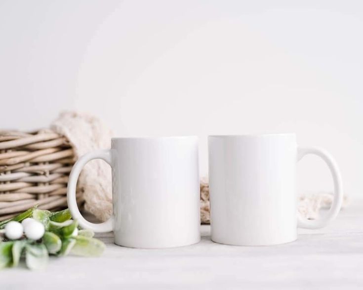 two white coffee mugs sitting on top of a table next to a wicker basket