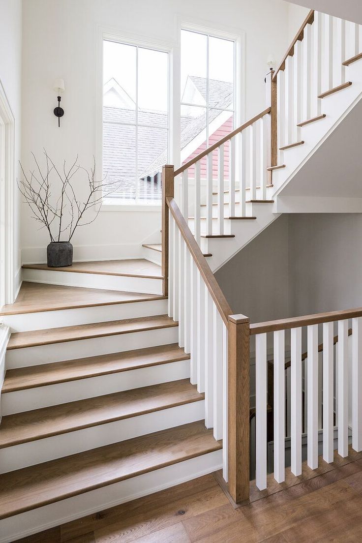 a white staircase with wooden handrails and wood flooring next to a potted plant