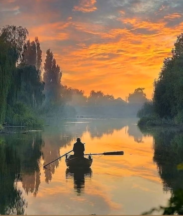 a man in a row boat on a river at sunset