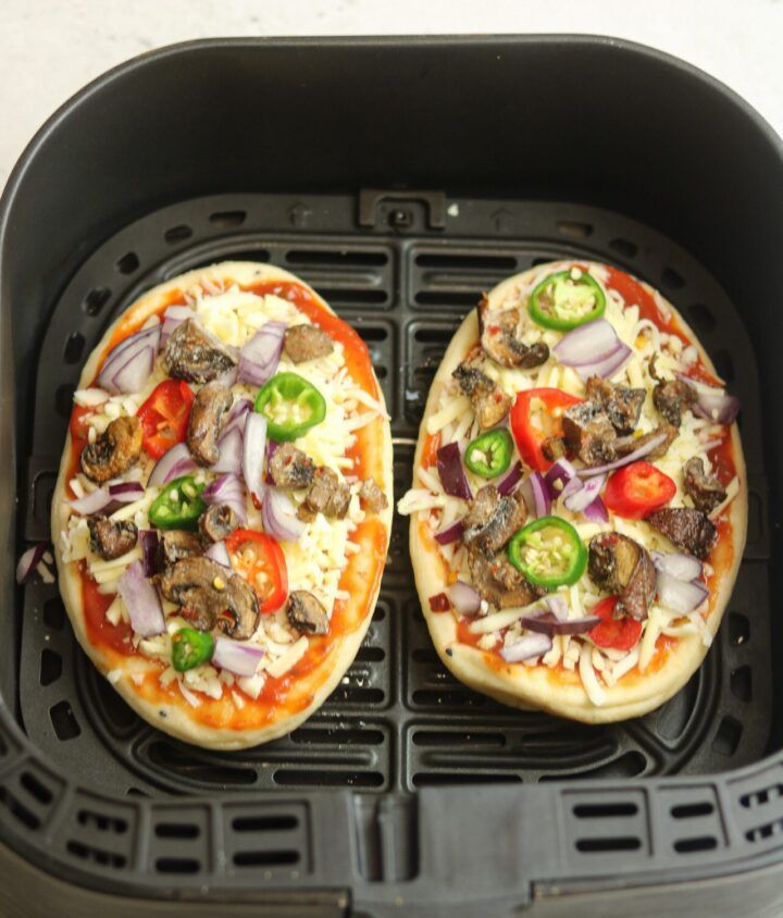 two pizzas sitting on top of a black grill