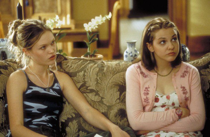 two young women sitting on a couch in front of a vase with flowers behind them