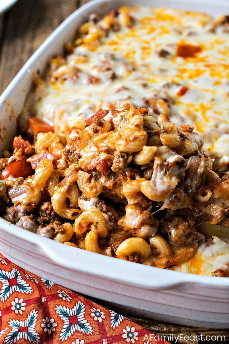 a casserole dish filled with pasta and meat in a white baking dish on top of a colorful cloth