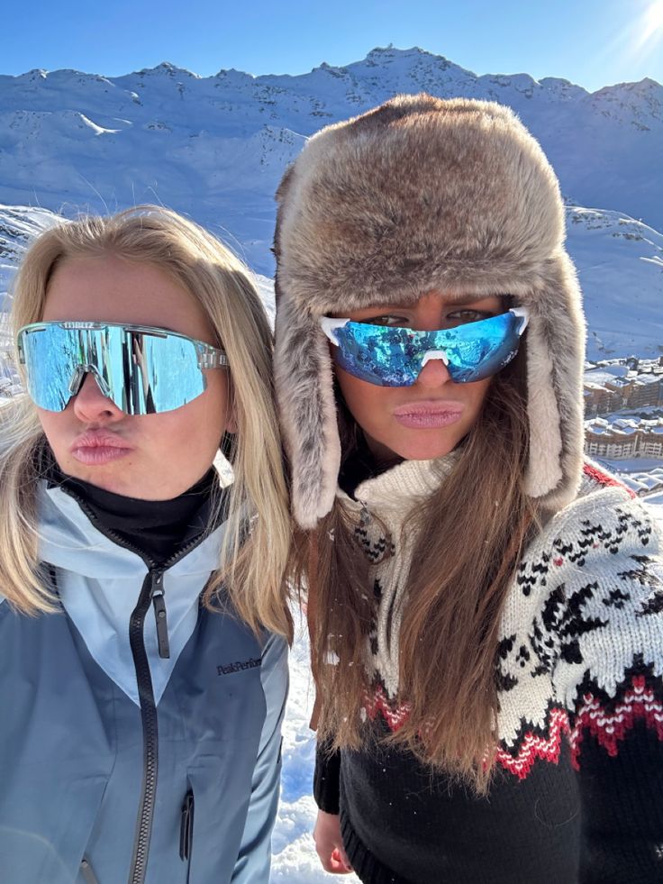 two women wearing ski goggles and hats in the snow