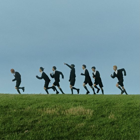 a group of people in suits running across a field on top of a grass covered hill