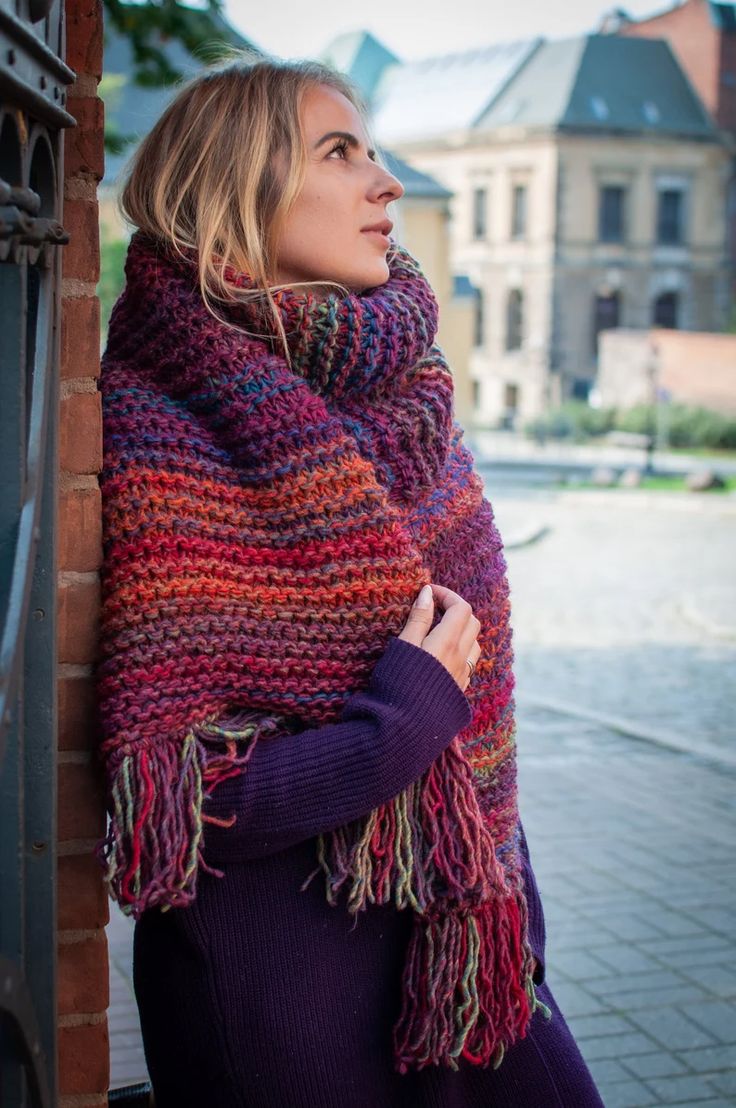 a woman wearing a multicolored shawl leaning against a brick wall