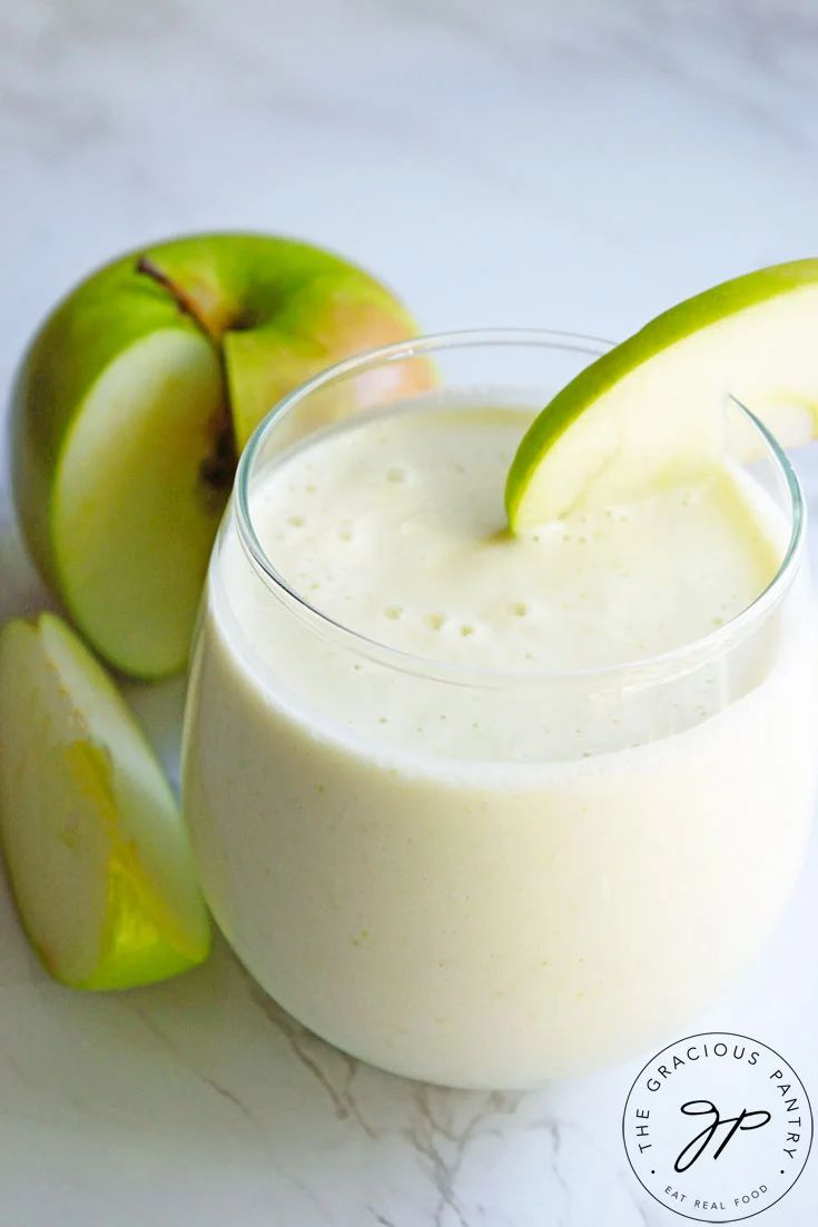 an apple and banana smoothie in a glass next to sliced apples