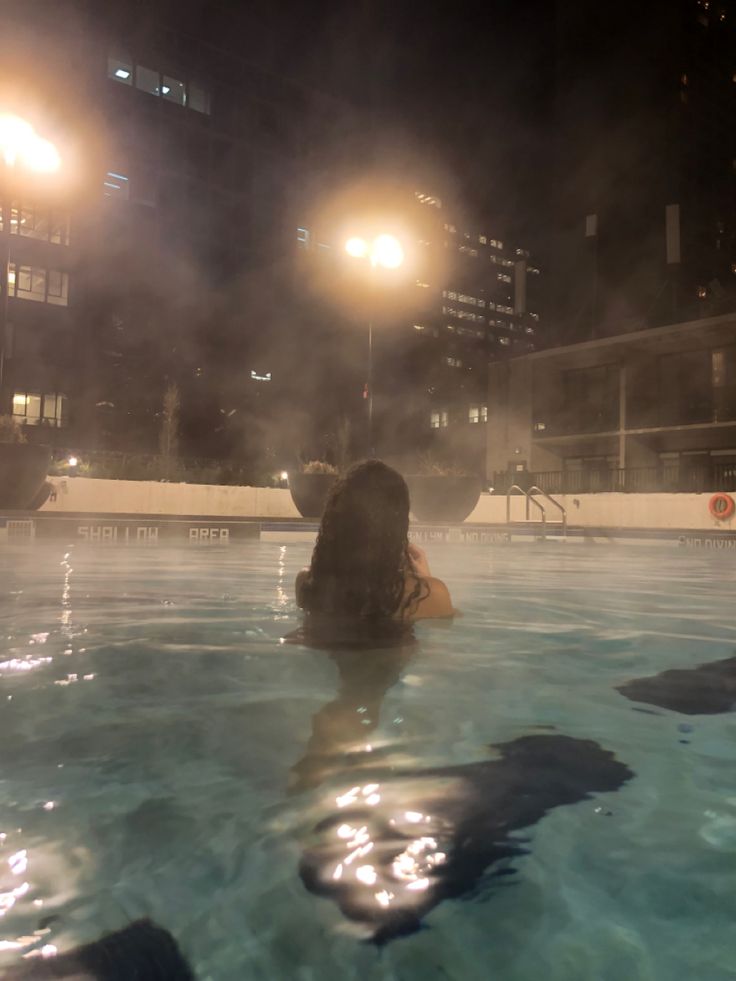 a woman sitting in the middle of a swimming pool at night with lights shining on her