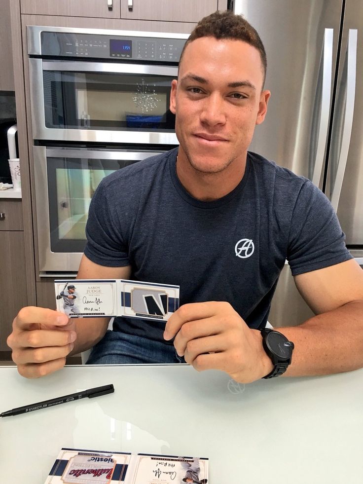 a man sitting at a kitchen counter holding up a camera and some cards in front of him