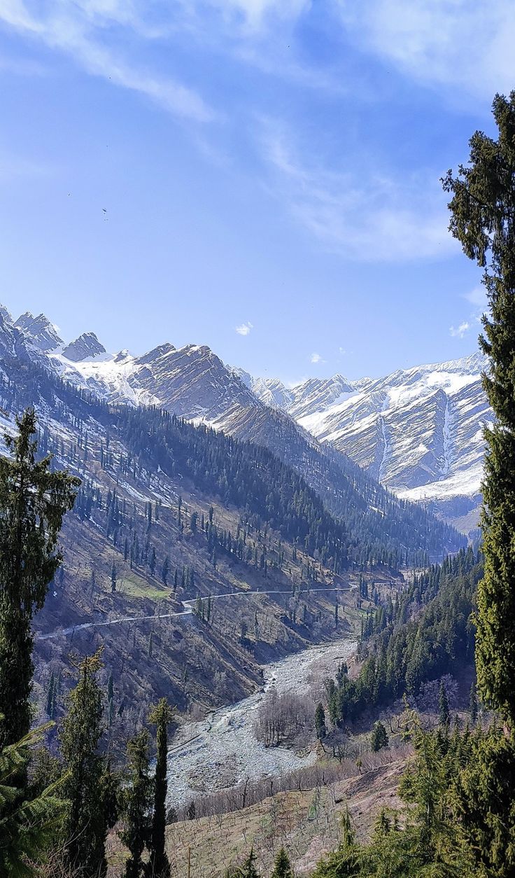 the mountains are covered in snow and have some trees on each side, with a river running through them