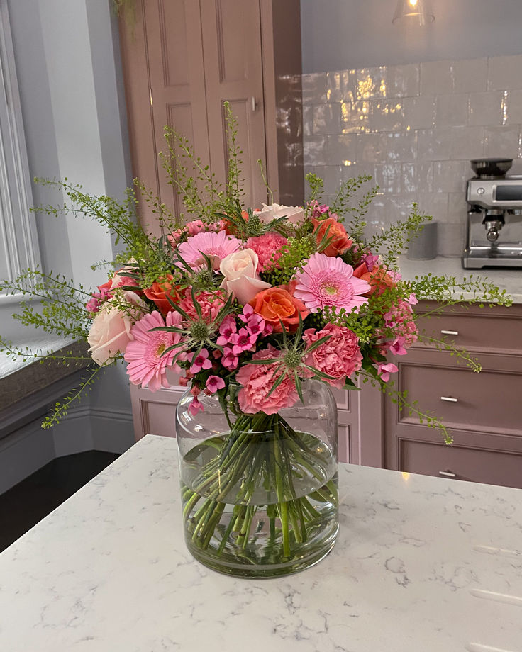 a vase filled with pink and red flowers on top of a kitchen counter next to an oven