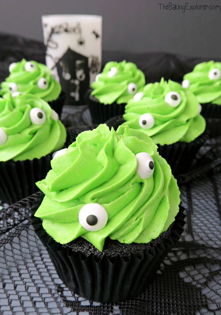 cupcakes with green frosting and googly eyes are on a black table