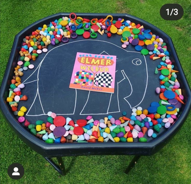 an elephant painted on top of a black table covered in colorful rocks and plastic beads