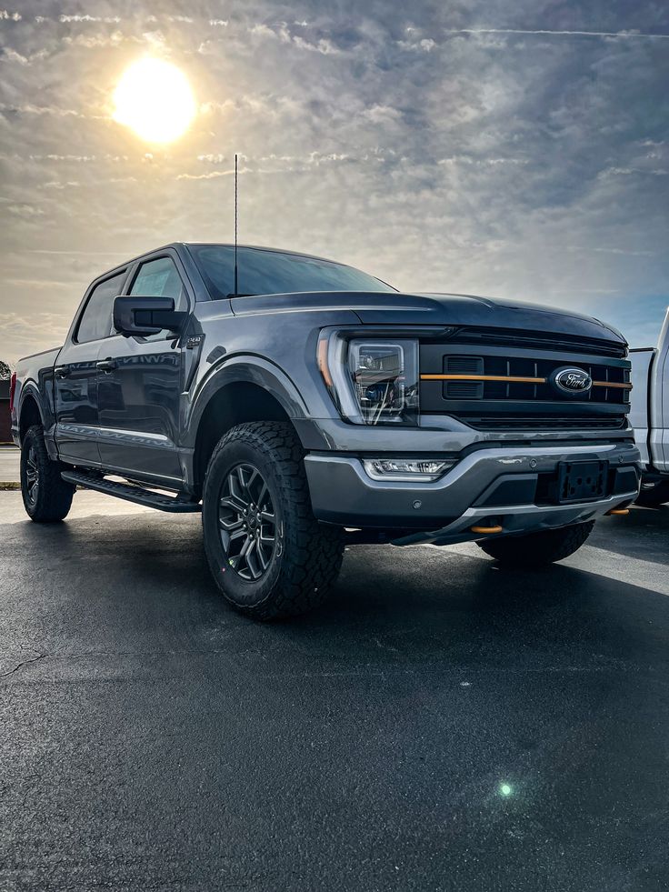 two trucks parked in a parking lot with the sun shining behind them and cloudy skies