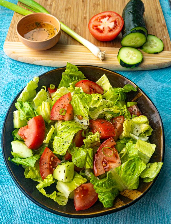 a salad with tomatoes, lettuce and cucumbers on a blue table cloth