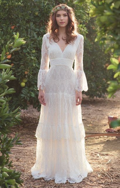 a woman wearing a white dress standing in the middle of trees and bushes with her hands on her hips