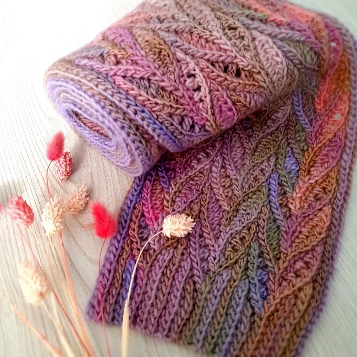 a knitted scarf sitting on top of a table next to dried flowers and twigs