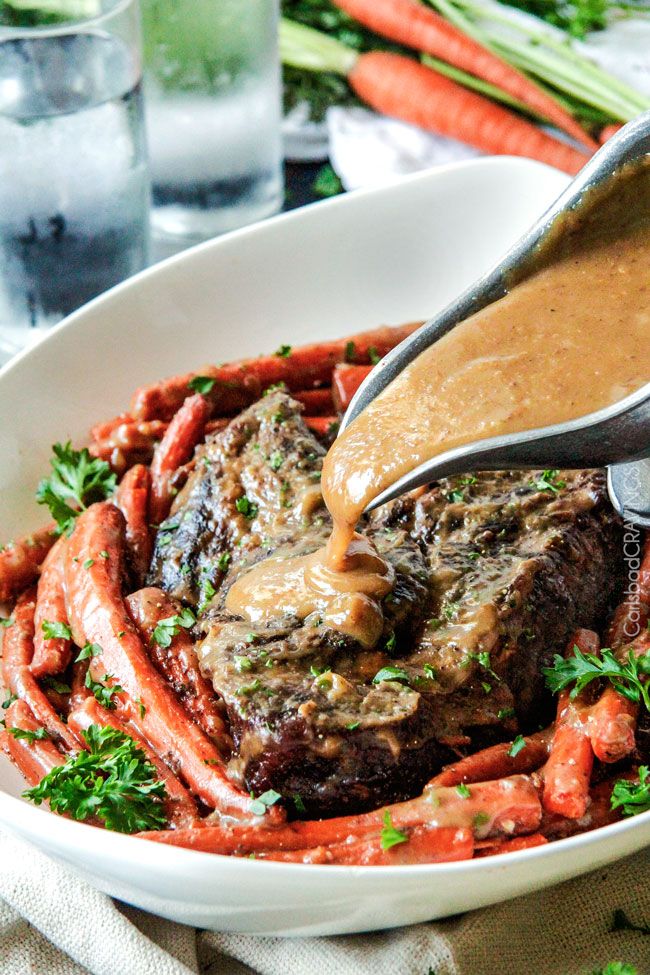 someone is pouring sauce on some meat and carrots in a white bowl with parsley