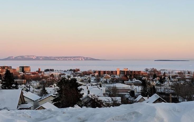 a view of some houses and the ocean in the distance with snow on the ground