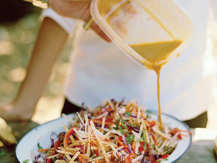 a person pouring dressing over a salad in a white bowl on top of a table