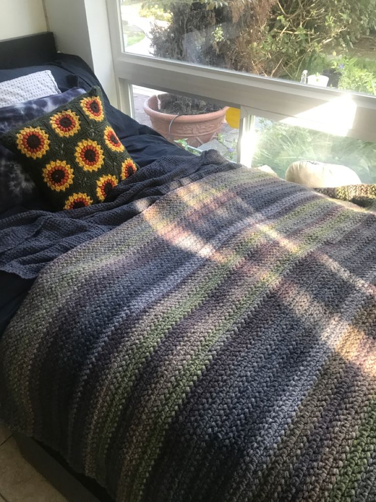 a bed with a blanket and pillows on top of it next to a large window