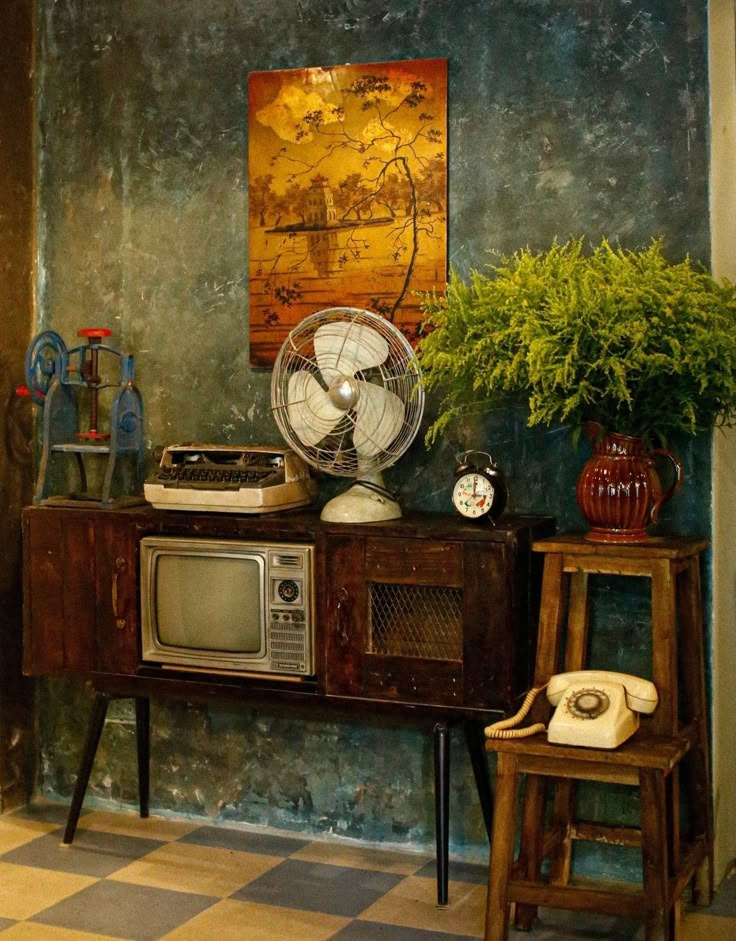 an old fashioned television sitting on top of a wooden cabinet next to a table with a fan