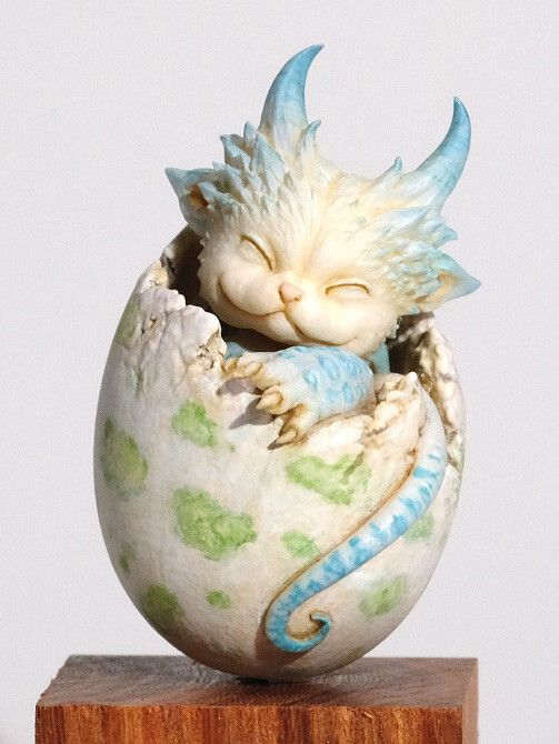 a ceramic figurine of a cat curled up in an egg with its eyes closed