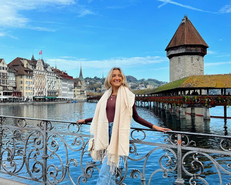 a woman standing on a bridge next to water with buildings in the background and blue sky