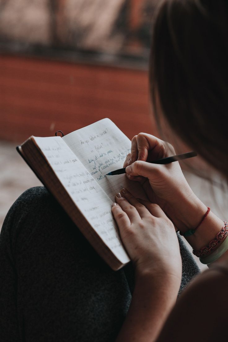 a woman writing on a notebook with a pen