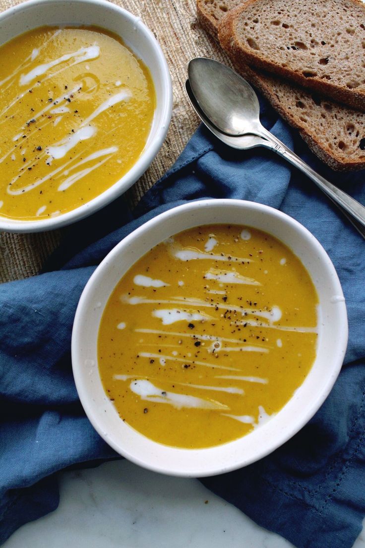 two bowls filled with soup next to slices of bread on top of a blue towel