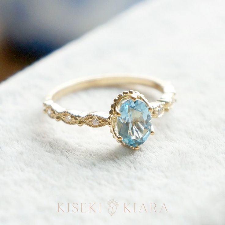 a gold ring with an aqua blue topazte in the center on a white surface