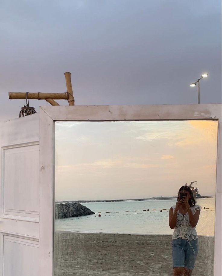 a woman taking a selfie while standing in front of a mirror on the beach