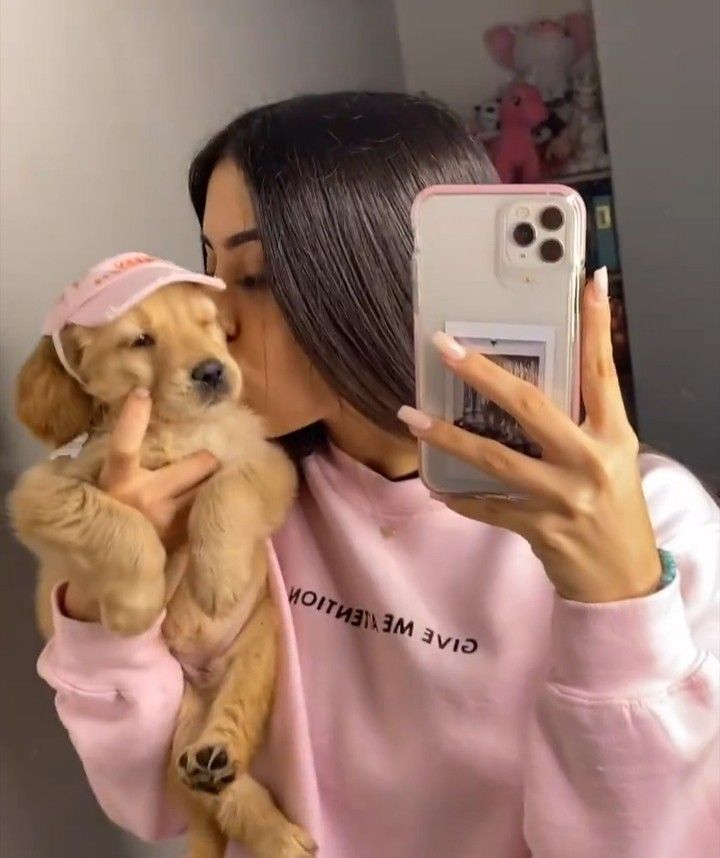 a woman taking a selfie with her cell phone while holding a puppy in her lap